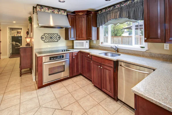 Traditional kitchen interior with wooden cabinets, granite countertop and stainless steel appliances.