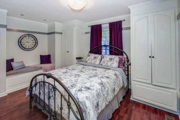 White and purple bedroom interior with iron bed, bench and built in cabinets.