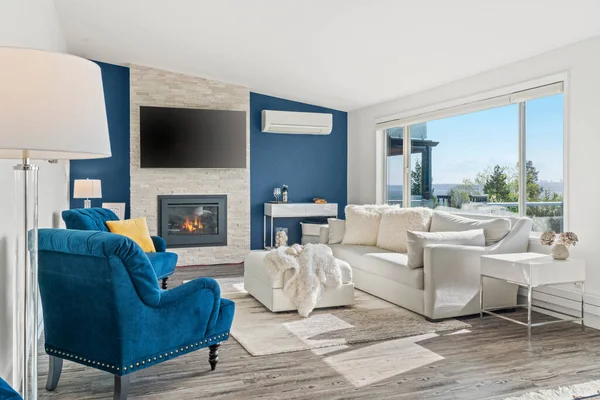 Welcoming living room with a blue accent wall, white faux fur pillows and a modern stacked stone fireplace