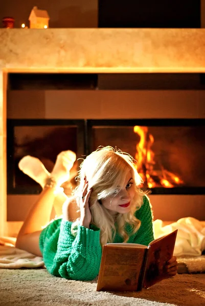 a warm blanket near the fireplace. Girl with a book by the fire. Firewood in the fireplace. woman in a warm knit sweater with books.