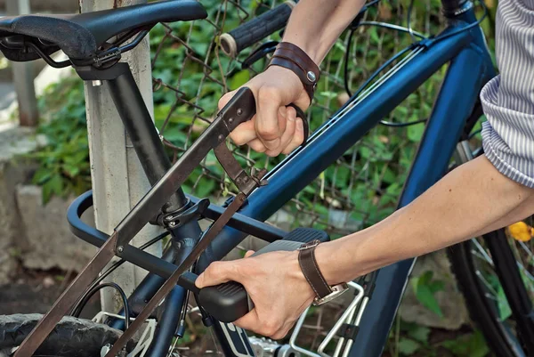 A man is hacking a bicycle lock with a saw