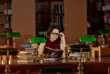 masada kitaplar ile gözlüklü esmer. Kütüphane tablolarda yeşil ışık yanarsa. Eski bir kütüphane ile kahverengi mobilya.