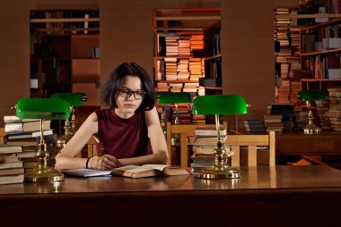 masada kitaplar ile gözlüklü esmer. Kütüphane tablolarda yeşil ışık yanarsa. Eski bir kütüphane ile kahverengi mobilya.