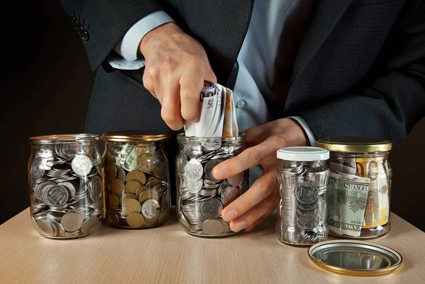 A man in a suit conserved money in glass jars. The concept is the storage of money, stocks at difficult times. Conserve money instead of vegetables.