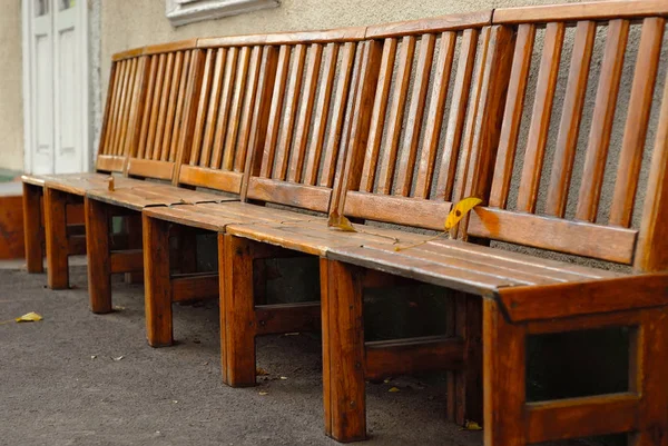 An old wooden bench in a park near a concrete wall.