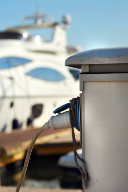 İskelede beyaz yatlar. Ön planda bir yat şarj etmek için bir kordon.