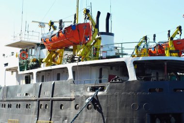 Kırmızı bir kurtarma teknesi limanda eski bir gemi üzerinde asılı.
