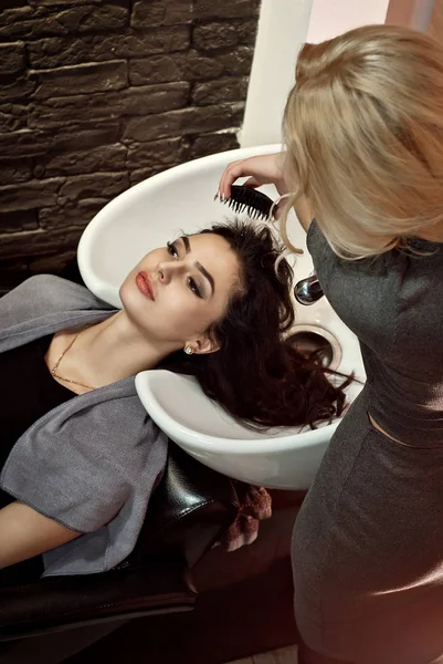 美容院的女孩主造型师清洁客户的头发 金发使黑发发型 美容院的客户服务愉快 — 图库照片