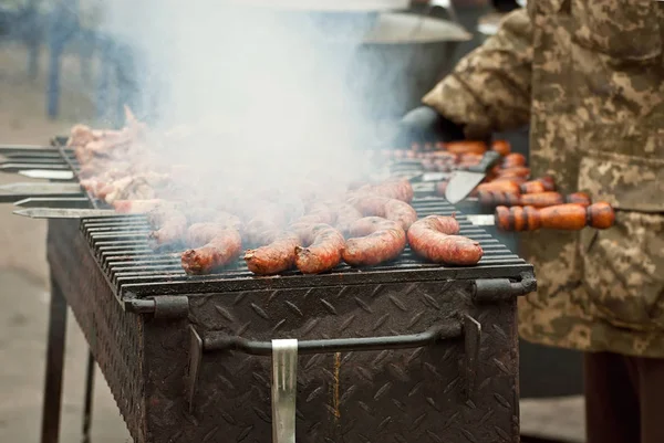 Cooking Grilled Meat. Servicemen prepare barbecue. A man in a military camouflage uniform fry the meat. Rest of the military at the festival. Army cuisine at the training ground.