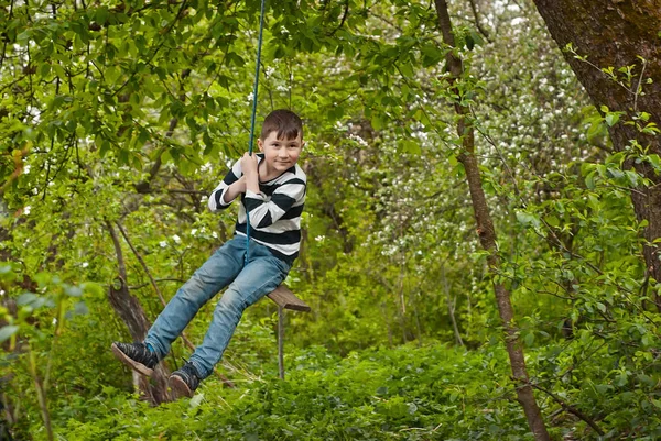 Children are riding a swing in the park. Guys on a homemade swing from ropes and boards. Light blur as an artistic effect of motion.