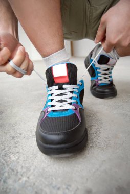 Şort ve spor ayakkabılı bir adam mermer kiremit giyiyor. Gri bir duvarın arka planında spor ayakkabıların yakın çekimleri. Atlet bağcıkları bağladı..