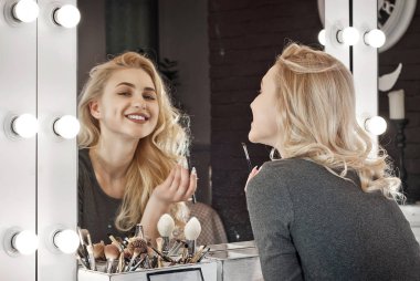 Kız bir arka ışık ile aynanın yanında bir makyaj yapar. Bir güzellik salonunda güzel bir sarışın.