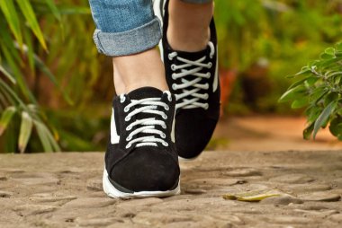 Kadın bacakları yakın çekim. Yeşil bitkilere karşı asfalt spor spor ayakkabıları. Tropikal iklim aranjör ayakkabı.