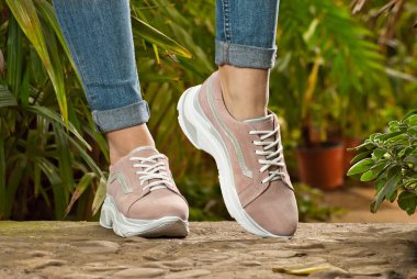 Kadın bacakları yakın çekim. Yeşil bitkilere karşı asfalt spor spor ayakkabıları. Tropikal iklim aranjör ayakkabı.