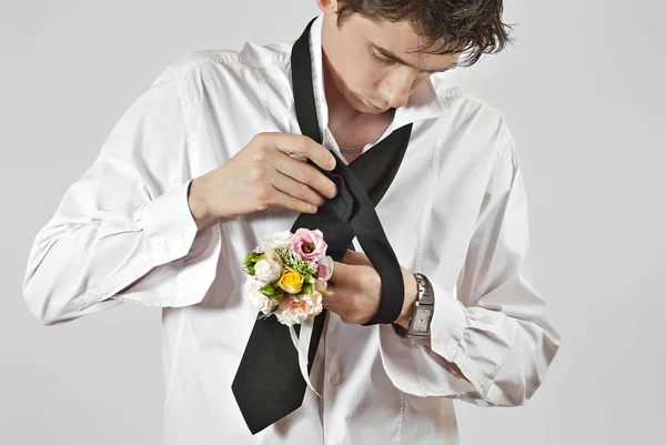 男はネクタイを結んだ 結婚式の日の準備 男はネクタイに結び目をつけるのを習っている 白いシャツに黒のネクタイ 手にたくさんの花が白い背景に孤立している — ストック写真