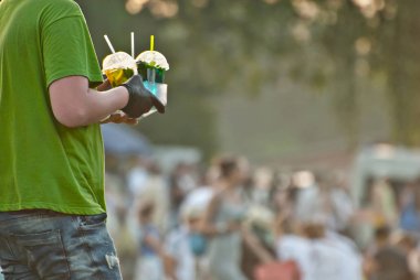 Çok renkli meyveli içecekler yakın çekim. Bir adamın festivalde plastik bardaklarda alkolsüz içecekleri var. Meyve suyu ve yeşillikli kokteyller.