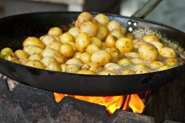Büyük bir tavada patates kızartması. Festivalde nefis yemekler. Mutfak ocakta. Genç yuvarlak patatesler yağda kızartılır..