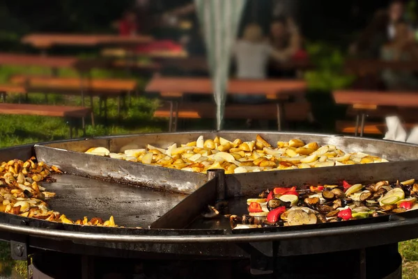 Vegetables fry on a large frying pan on fire. Cooking at the festival.