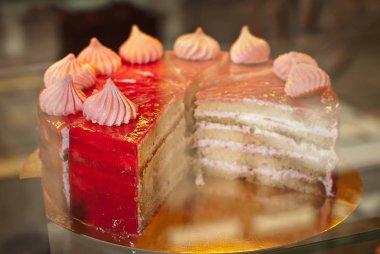 Bir dükkan penceresinde kırmızı doldurulmuş yuvarlak pasta. Pastanın üzerine marshmallow. Kek parçalara ayrılmış.