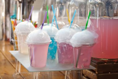 Çok renkli meyveli içecekler. Festivalde plastik bardaklarda alkolsüz içkiler. Meyve suyu ve sebzeli kokteyl. Beyaz duman kokteyllerle buharlanıyor..