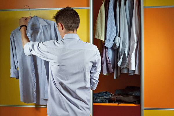 Мужчина в полосатой рубашке примеряет одежду на заднем плане шкафа. Желтый и оранжевый шкаф. Парень подбирает костюм. Концепция выбора одежды
.