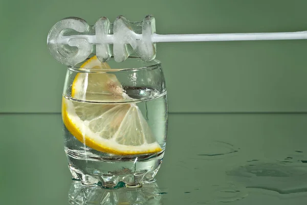 Alcoholic drink with lemon in clear glasses. Little cup isolated on green background. Frozen drinks on glass table. Ice in the form of an inscription - \