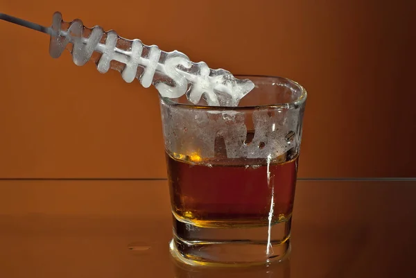 透明なグラスに氷を入れたアルコール飲料 オレンジ色の背景に分離されたカクテルとワイングラス ガラスのテーブルの上の冷凍ドリンク 碑文の形の氷 ウイスキー — ストック写真