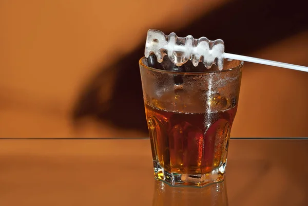 透明なグラスに氷を入れたアルコール飲料 オレンジ色の背景に分離されたカクテルとワイングラス ガラスのテーブルの上の冷凍ドリンク 碑文の形の氷 — ストック写真