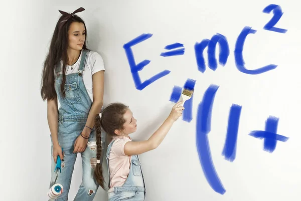 The girls paint the walls. Friendly collaboration between the two sisters. Teens in blue overalls make repairs together. Girlfriends write formulas in physics on the wall with blue paint.