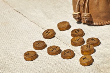 Wooden runes with symbols and alphabet close up. Pagan mascots are scattered on the table. clipart