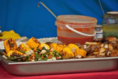 Bir sürü pişmiş mısır yakın. Festivalde masada sarı mısır var. Tabakta salata olan kavrulmuş mısır. Makarna, otlar ve fasulye ızgara vardır.