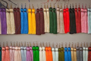 Fuarda renkli iplik küpeleri satılmaktadır. El yapımı takı bir ip üzerinde asılı.