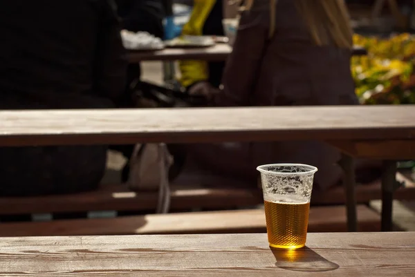 Beer in a plastic glass close-up. Alcoholic beverage at the festival. Glass on an old wooden table.