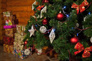 Tahta arka planda çelenkler ve katmanlarla süslenmiş Noel ağacı. Parlak ve ayna oyuncakları kapanıyor. Noel ağaçlarında çok renkli süslemeler. Arka planda bulanık hediye kutuları.