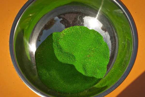 Green paint in powder form. Texture of fine powder in a metal bowl. Paint for children's creativity.