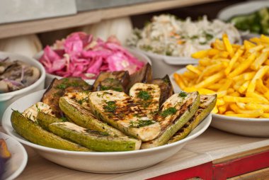 Sebzeler büyük bir tavada ateşte kızarıyor. Festivalde yemek pişirmek. Masadaki tabakta kızarmış kabak..