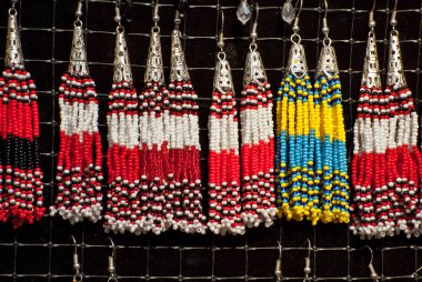 Fuarda renkli iplik küpeleri satılmaktadır. El yapımı takı bir ip üzerinde asılı.