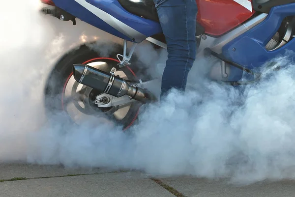 The smoke comes out from under the wheels. Motorcycle wheel closeup. Smoke due to tire rubbing against asphalt. The rider prepares to do the trick on the motorcycle. Burned rubber on the road.