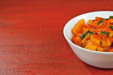 Tahta bir masada beyaz bir tabakta patates. Kırmızı tahtada portakal soslu haşlanmış patates. Yazı için plakaya yakın bir yere. Tasarım için alanı kopyala.