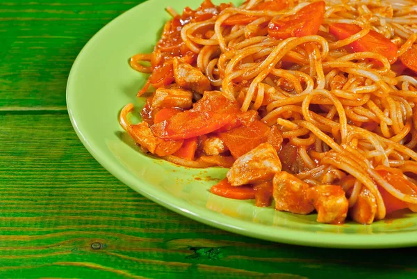 Pasta with carrots and meat in a green plate on a wooden table. Vermicelli with orange sauce on a shabby board.