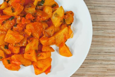 Tahta bir masada beyaz bir tabakta patates. Portakal soslu haşlanmış patates.. 