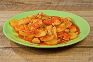 Tahta bir masada yeşil tabakta patates. Portakal soslu haşlanmış patates..