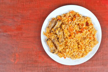 Beyaz tabakta et ve havuçlu pilav. Kırmızı kontrplak üzerine pirinç. Yemek yakınında metin ve kopyalama alanı.