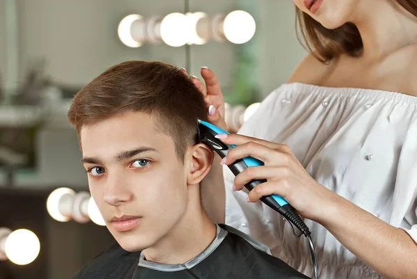 The hairdresser cuts the guy with a hair clipper. Head close up. Place for text near the models. Layout for design, copy space. Customer in a black cape on a background of yellow light bulbs.