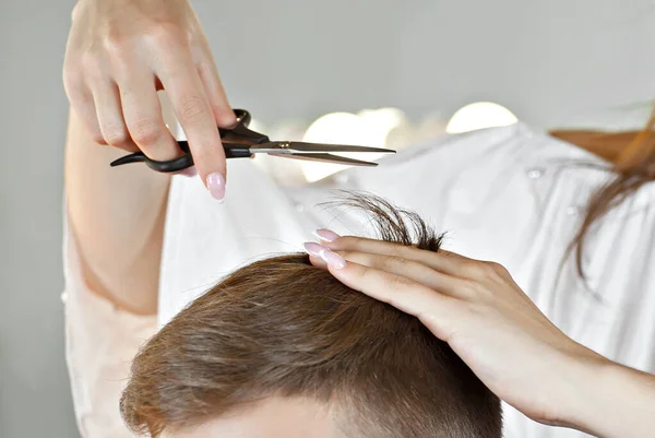 The girl makes a hairstyle to the guy. Hairdresser in a beauty salon with scissors in hand. Client and hairdresser on a white background.