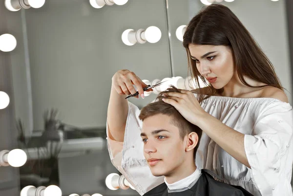 The girl makes a hairstyle to the guy. Hairdresser in a beauty salon with scissors in hand. Client and hairdresser on a white background.