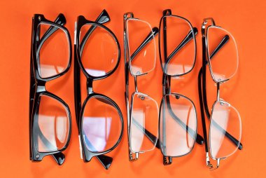 Turuncu arka planda farklı tipte gözlükler var. Dikdörtgen ve yuvarlak çerçeveli gözlük.