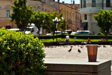 Kentsel mimarinin arka planında kahverengi kağıt bardak. Mermer sınırında kahve. Eski kasabanın evleri arka planda bulanıklaşıyor. Kahvede keskinlik. Tasarım için düzenName.