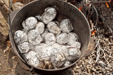 Dökme demir bir kazanda pişirilmiş folyoda patates. Kamp ateşinde yemek pişirmek..