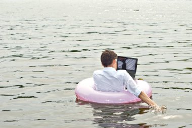 Pembe şişme dairede tişörtlü bir adam. Dizüstü bilgisayarı olan adam nehirde yüzüyor. Tatil, taşeronluk ve serbest çalışma kavramı. İş adamının yanında metin ve kopyalama alanı.